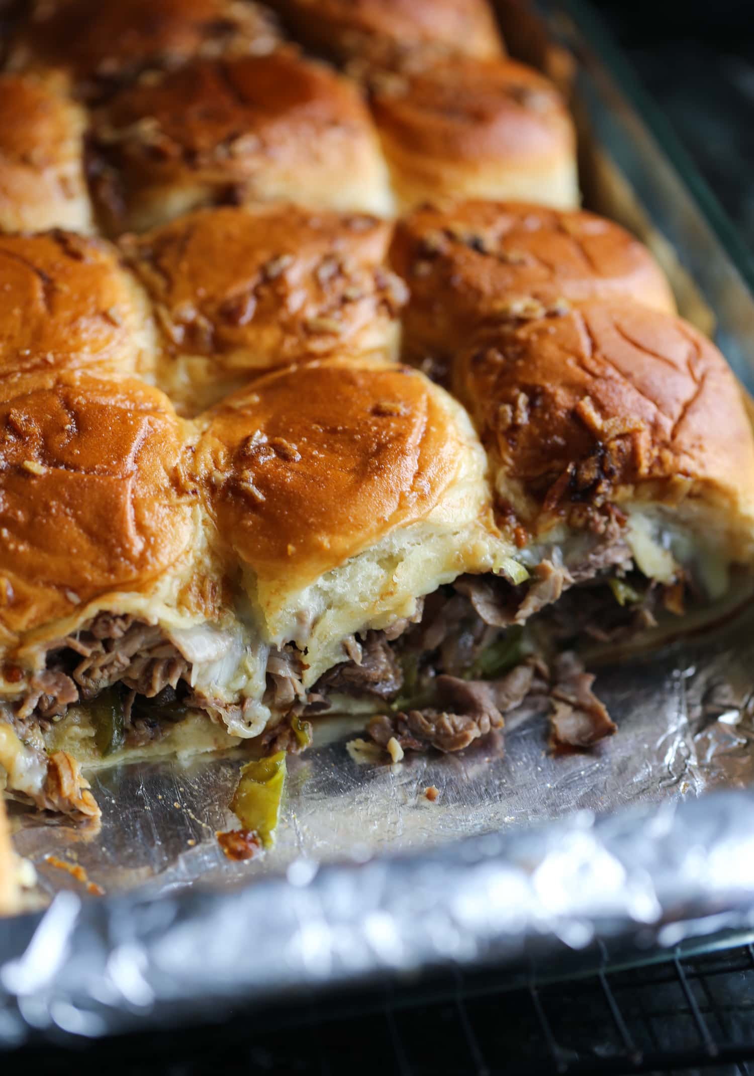 Philly cheesesteak sliders in a baking dish with one row missing.