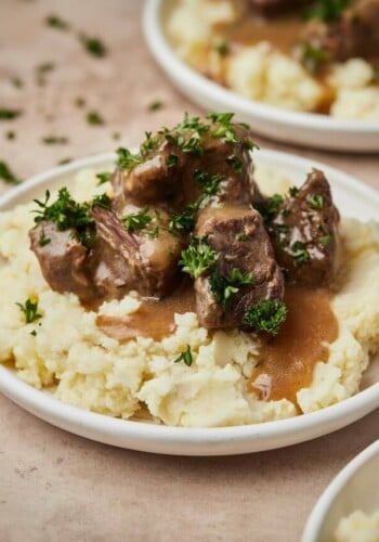 Instant Pot cubed beef and gravy served over a bed of mashed potatoes on a plate.