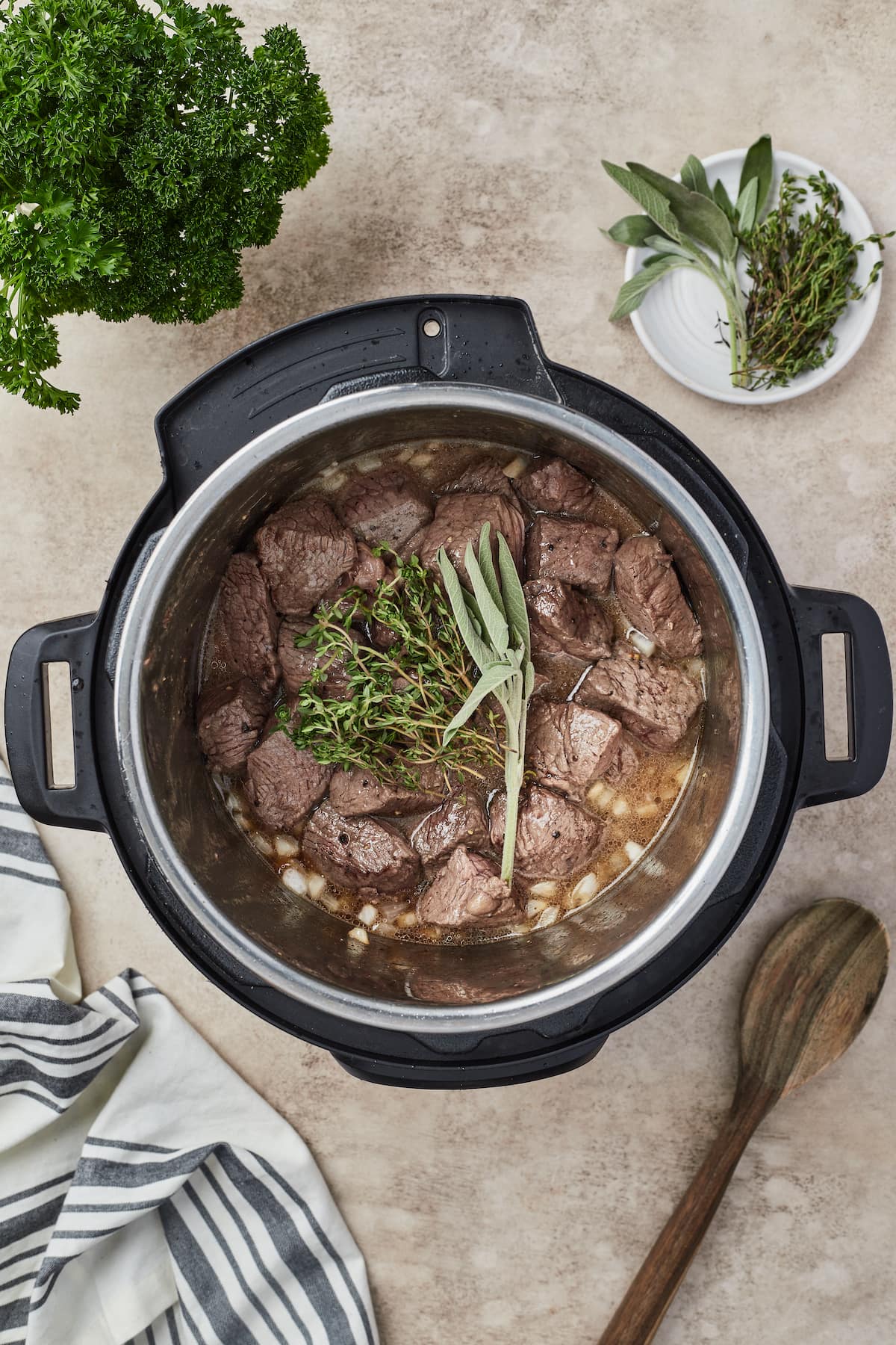 Browned beef chunks are added to an Instant Pot with onions, garlic, and herbs.