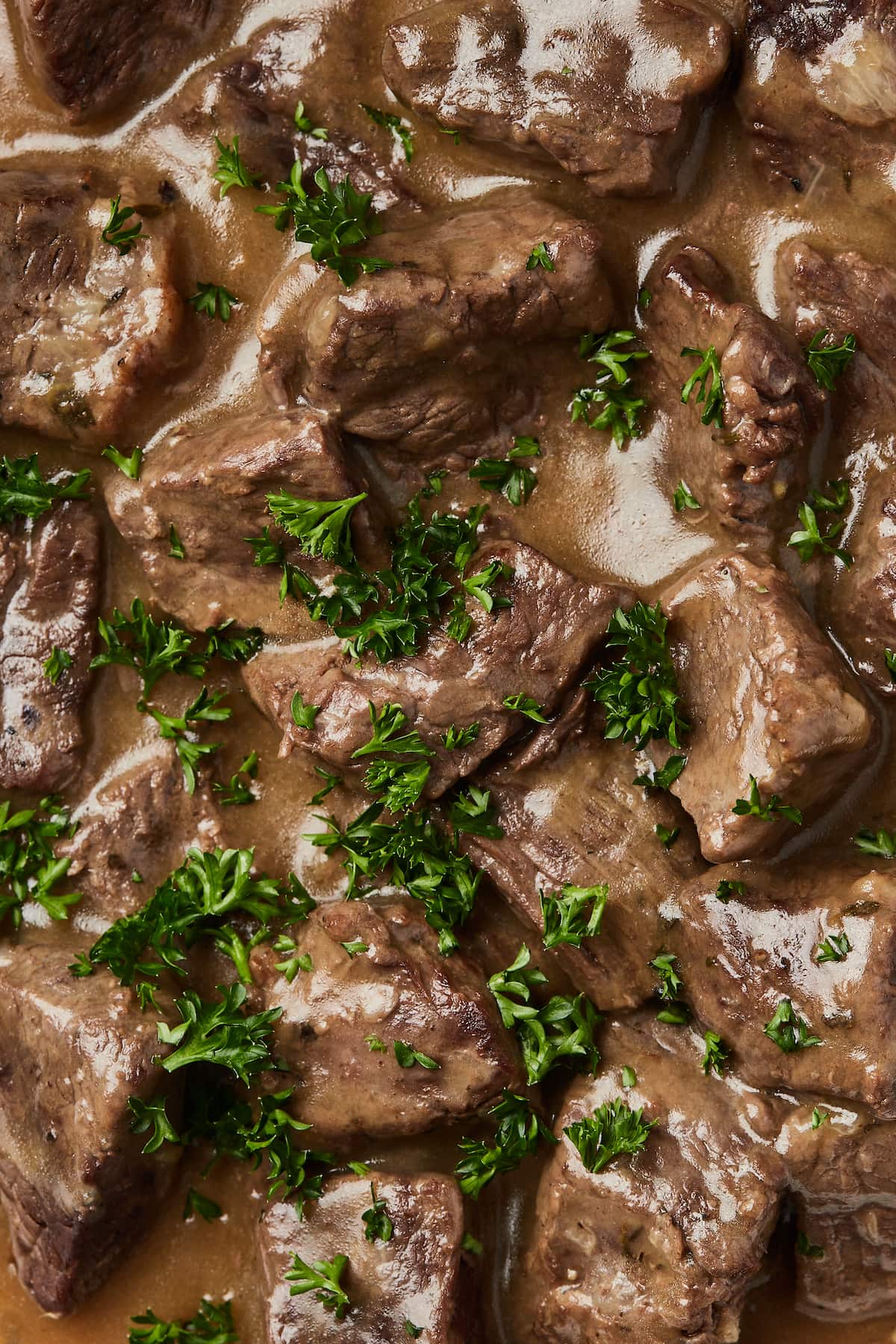 Close up of Instant Pot cubed beef soaked in gravy and garnished with fresh chopped parsley.