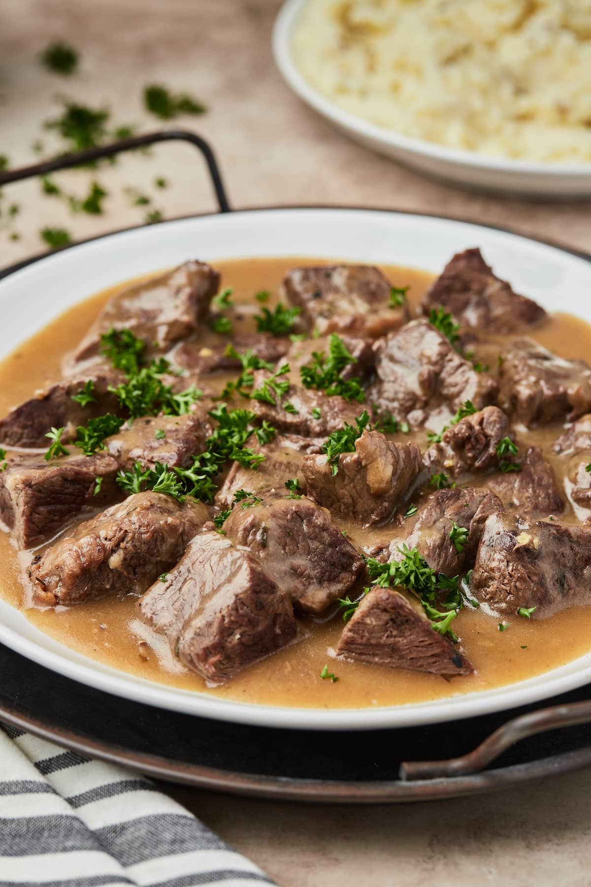 Cubed beef covered with gravy on a round serving dish garnished with green parsley.