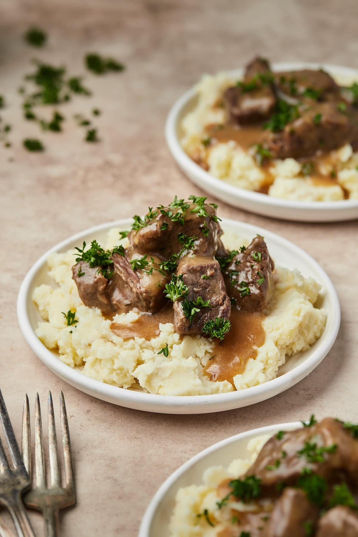 Plates of Instant Pot cubed beef and gravy served over mashed potatoes.