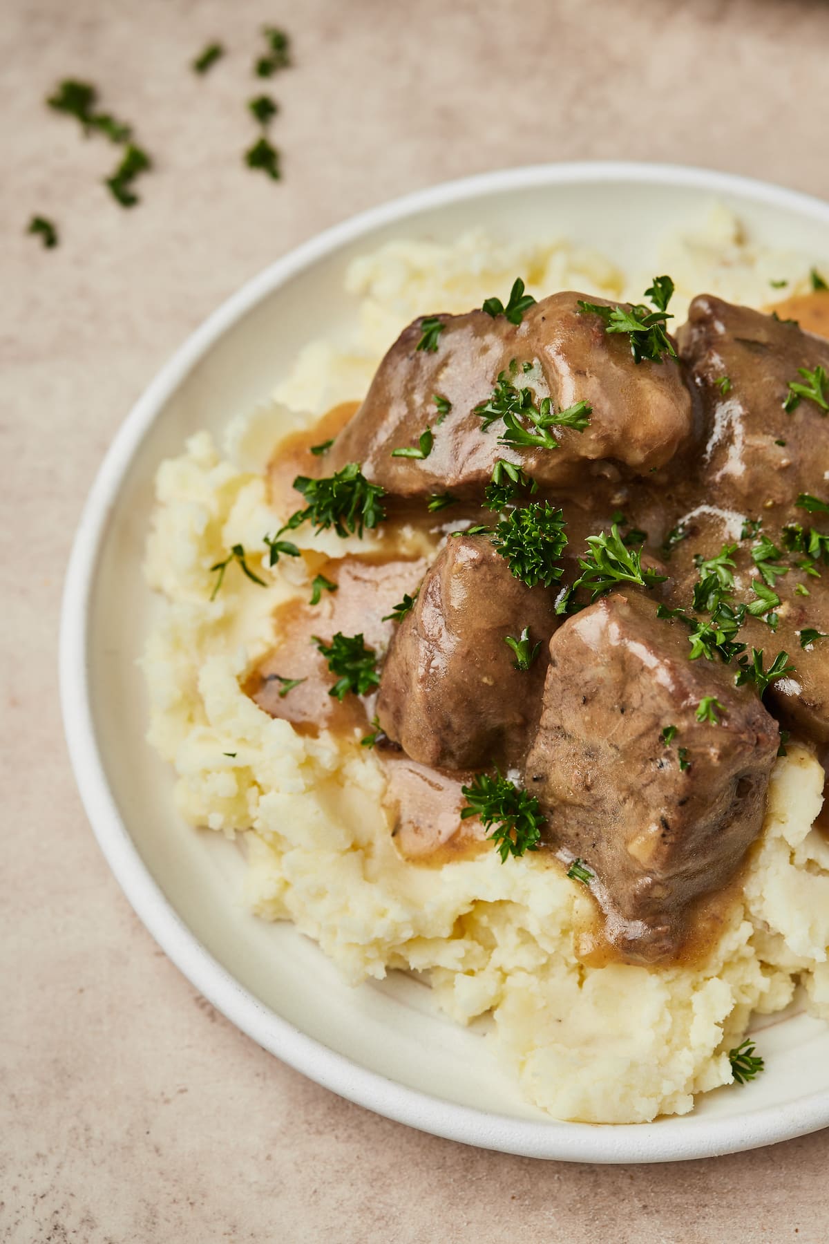 Instant Pot cubed beef and gravy served over a bed of mashed potatoes on a plate.