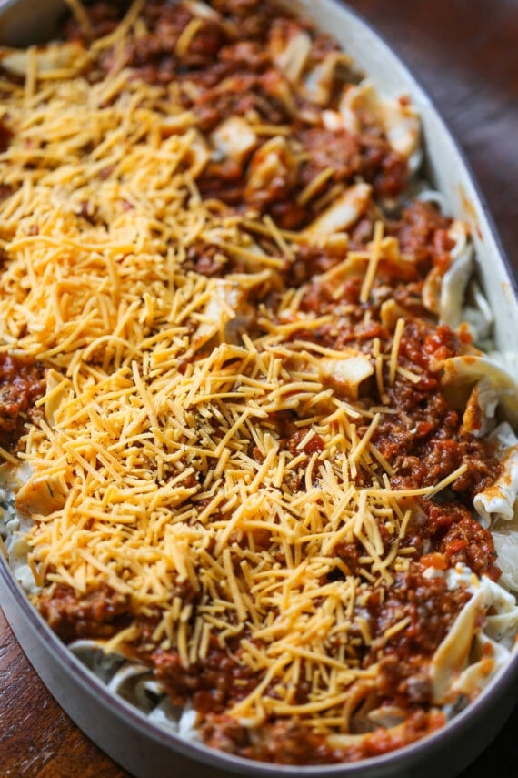 Layers of sour cream noodle bake are topped with shredded cheese in a casserole dish.