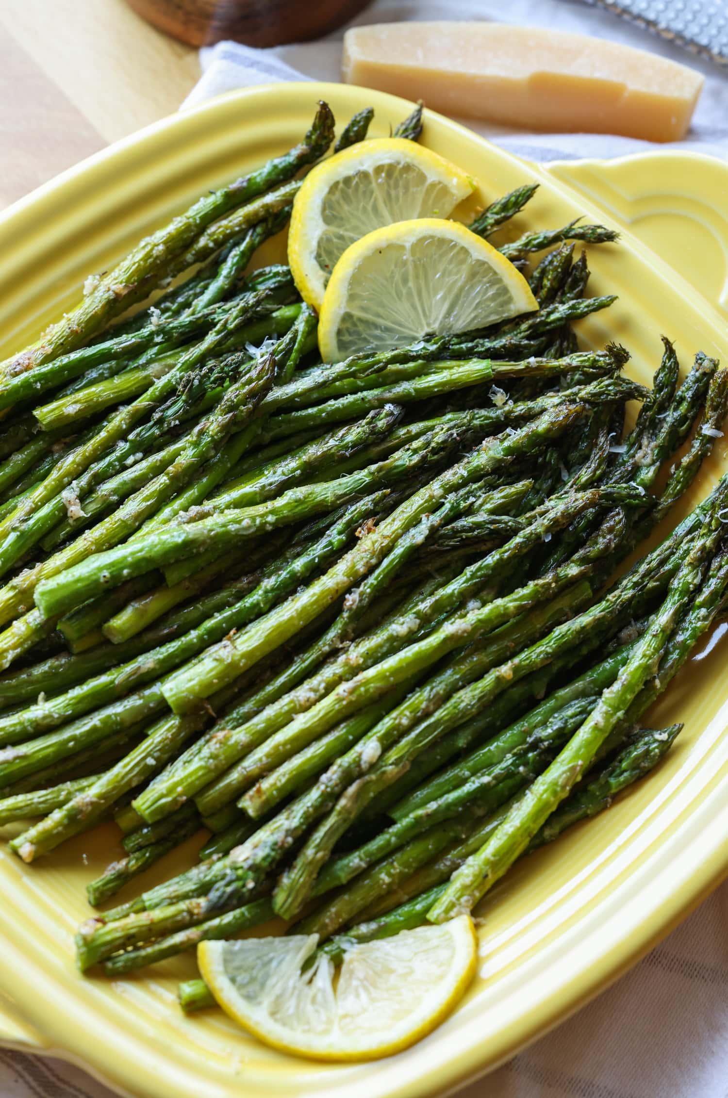 Roasted air fryer asparagus on a yellow square serving platter, garnished with lemon slices.