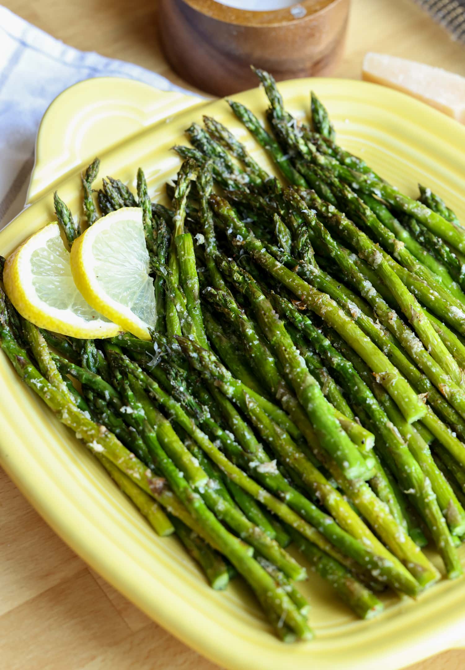 Roasted air fryer asparagus on a yellow square serving platter, garnished with lemon slices.