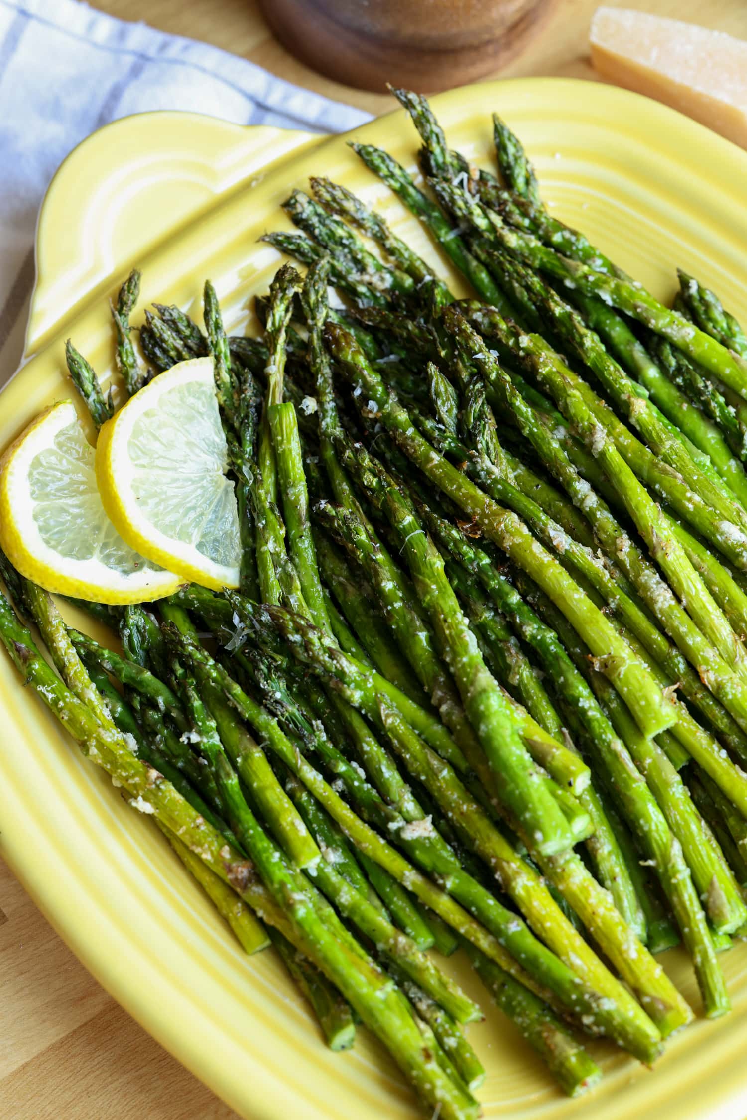 Roasted air fryer asparagus on a yellow square serving platter, garnished with lemon slices.