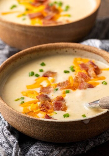 Two side-by-side bowls of loaded Instant Pot potato soup topped with shredded cheese, bacon bits, and chives.