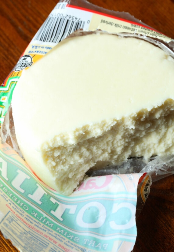 A partially crumbled wheel of cotija cheese resting on its wrapper.
