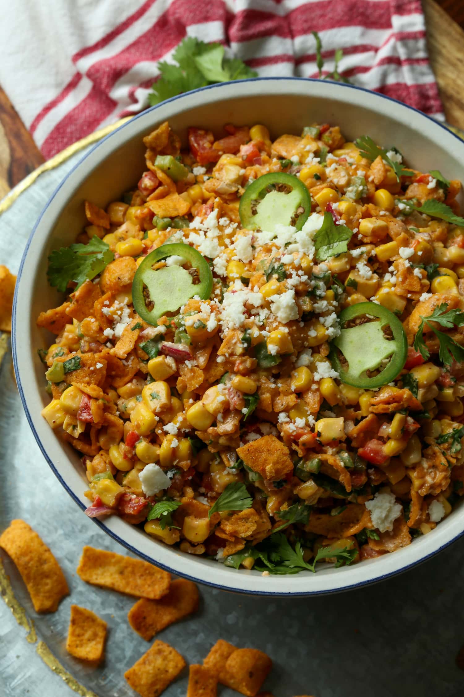 Spicy Frito corn salad topped with cotija cheese and sliced jalapeños in a large white salad bowl.