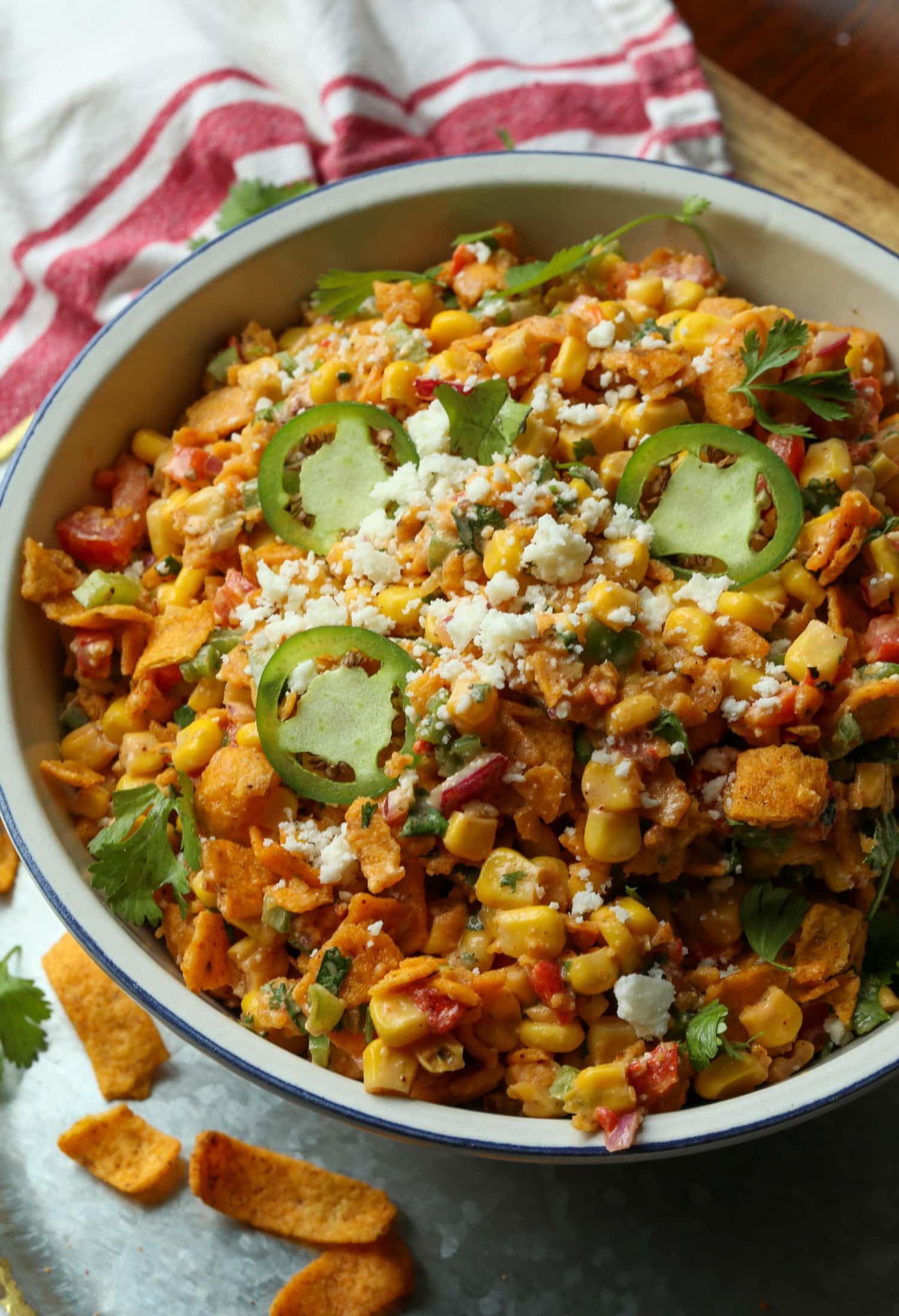 Spicy Frito corn salad topped with cotija cheese and sliced jalapeños in a large white salad bowl.