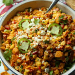 Spicy Frito corn salad topped with cotija cheese and sliced jalapeños in a large white salad bowl with a serving spoon.