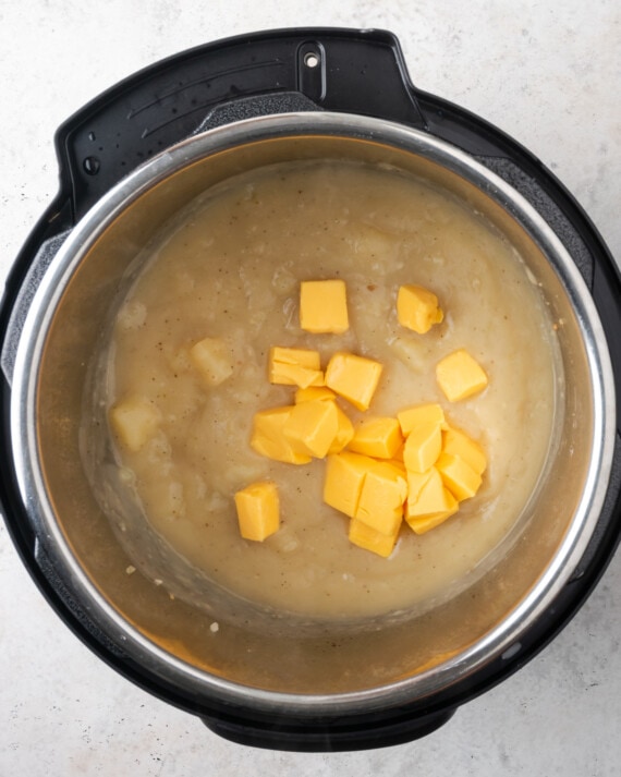 Chunks of orange cheese are added into the Instant Pot with the pureed potatoes.