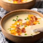 Two side-by-side bowls of loaded Instant Pot potato soup topped with shredded cheese, bacon bits, and chives.