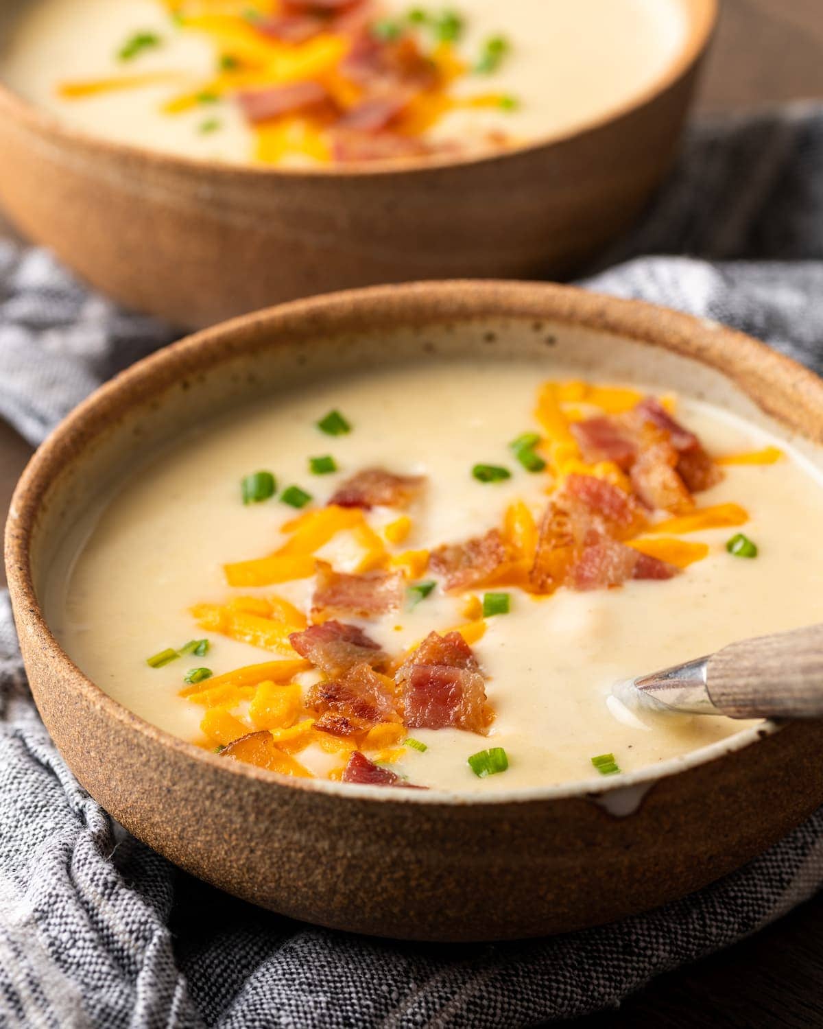 Two side-by-side bowls of loaded Instant Pot potato soup topped with shredded cheese, bacon bits, and chives.