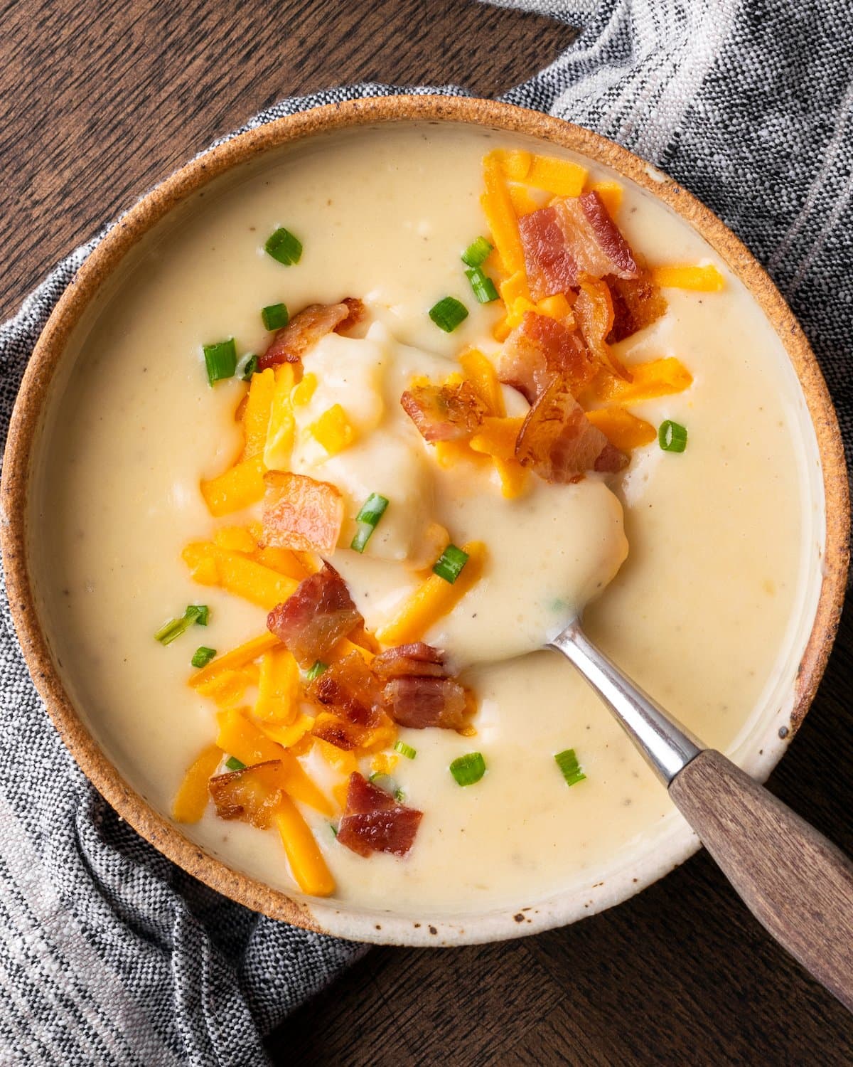 Top view of Instant Pot potato soup garnished with bacon, cheese, and chives, with a spoon.