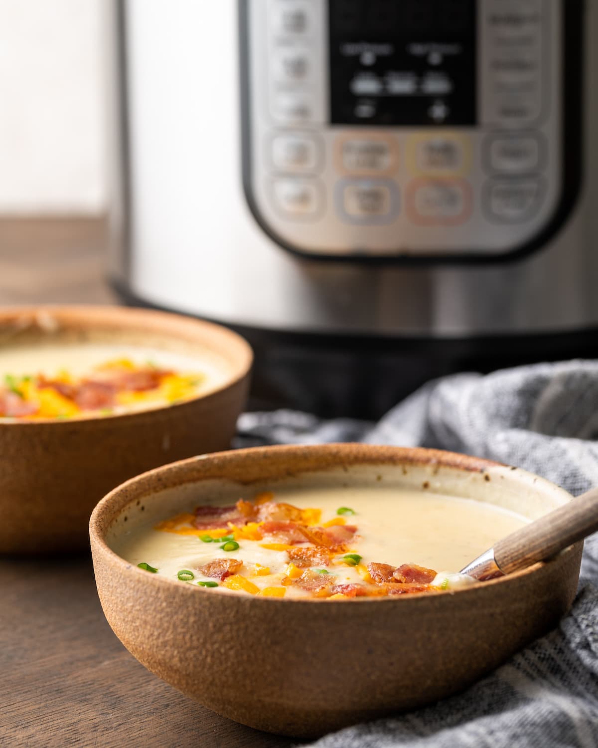 Two bowls of potato soup garnished with bacon, cheese, and chives with the Instant Pot in the background.