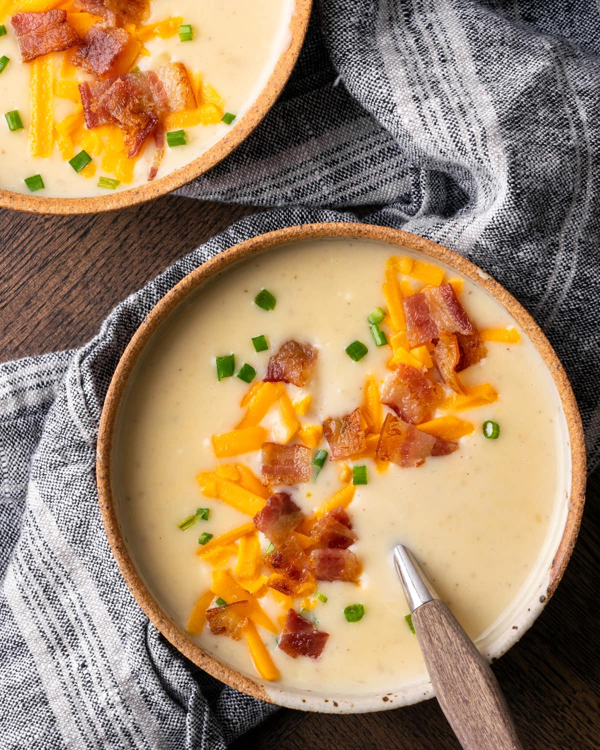 Top view of two side-by-side bowls of loaded Instant Pot potato soup topped with shredded cheese, bacon bits, and chives.