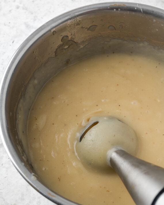 An immersion blender purees potatoes in a pot.