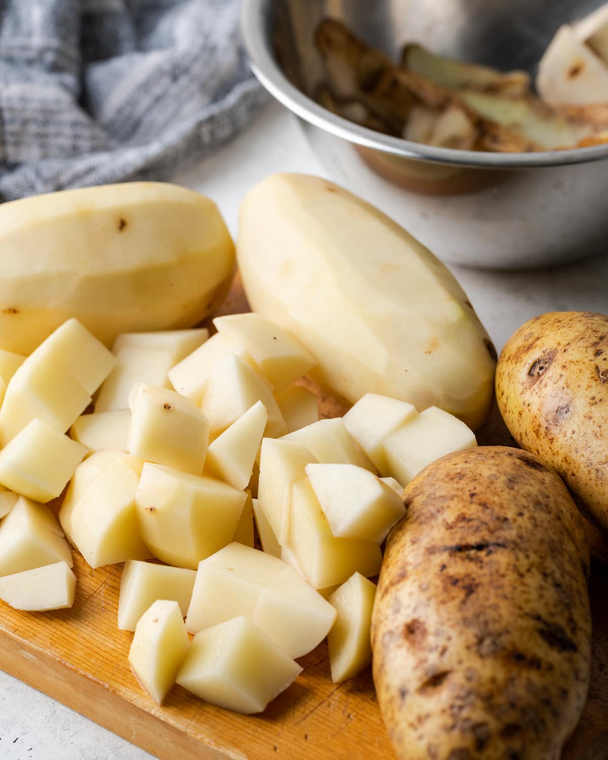 Chopped potatoes on a cutting board next to whole peeled and unpeeled potatoes.