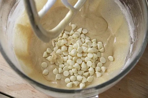 Overhead view of batter with white chocolate chips in a stand mixer bowl