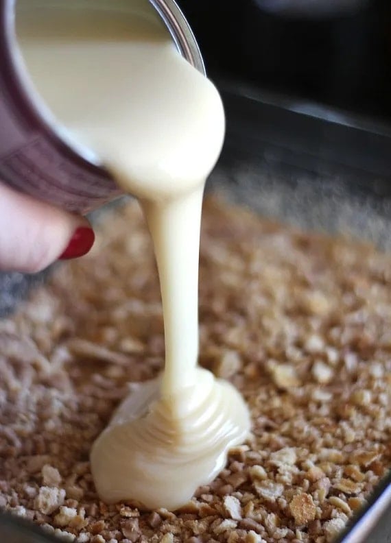 Sweetened condensed milk being poured over crushed Ritz crackers in a baking dish
