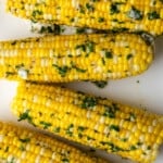 Top view of corn on the cob coated with butter and herbs.