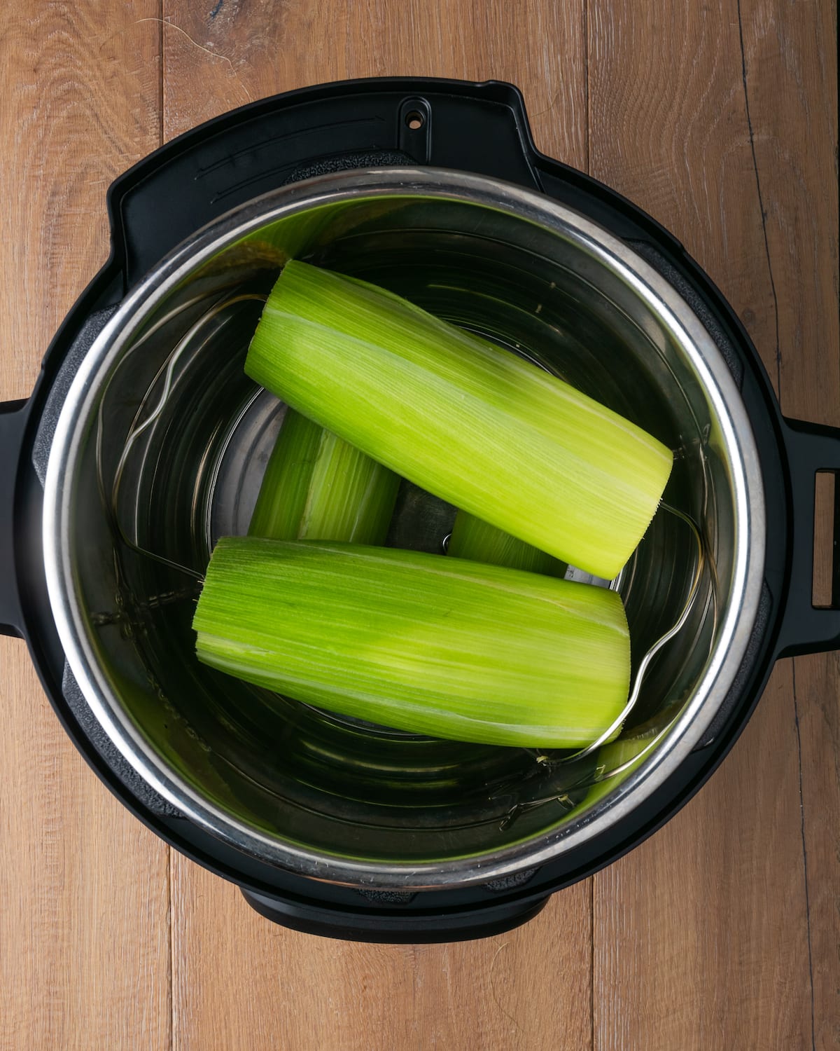 Top view of ears of corn with husks inside an Instant Pot.