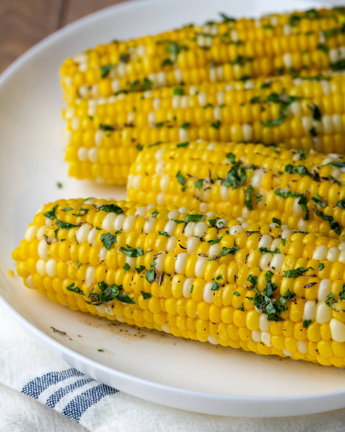 Corn on the cob coated with herb butter on a white plate.