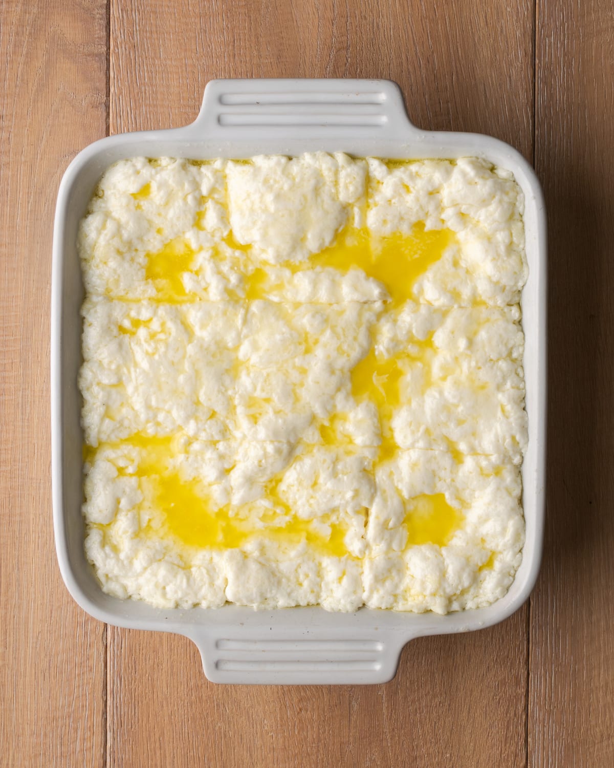 Butter swim biscuit batter in a square baking dish topped with more melted butter.