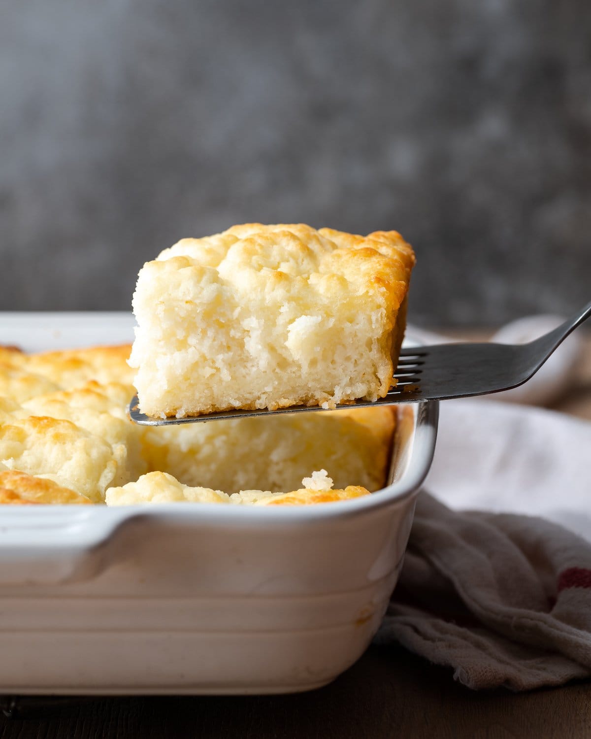 A butter swim biscuit is lifted from a white baking dish.