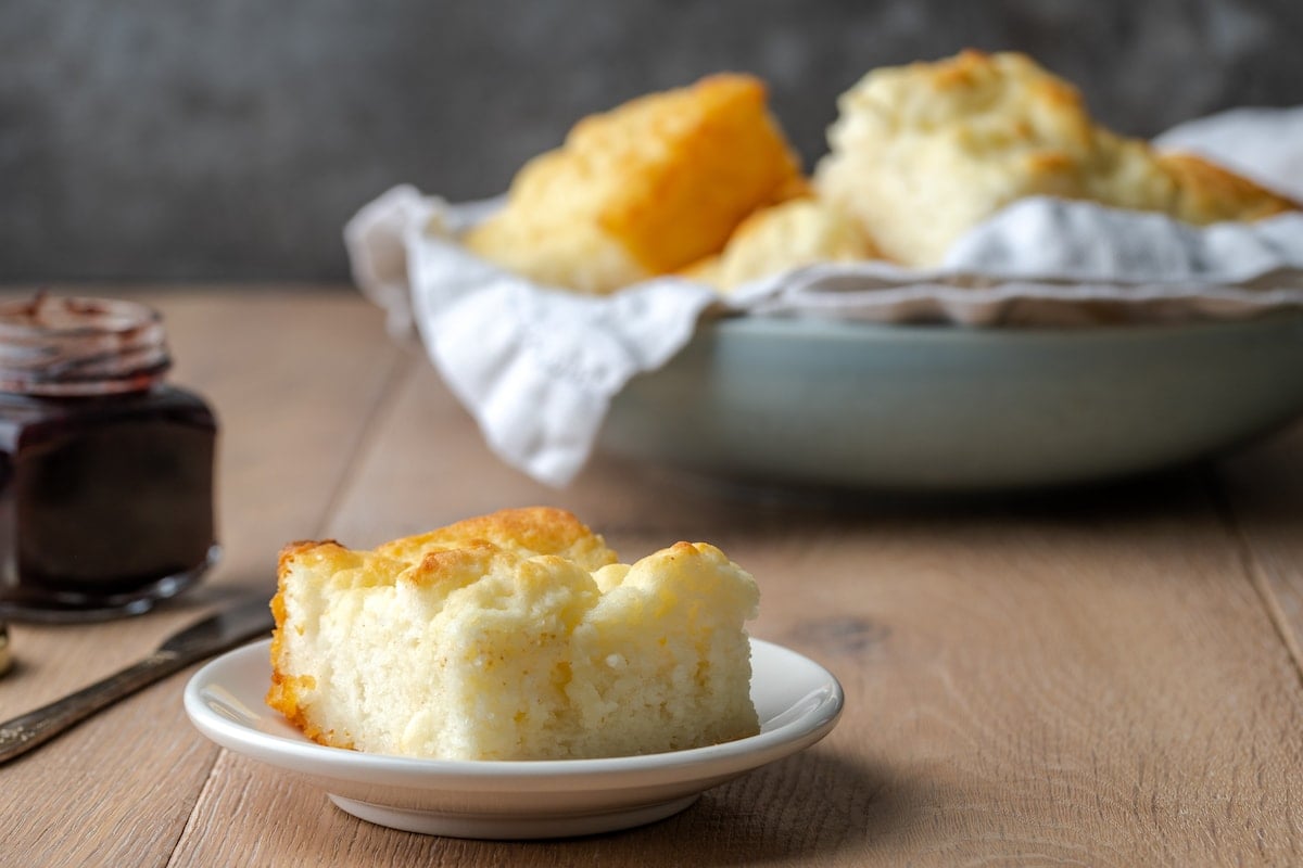 A single biscuit on a white plate, with more butter swim biscuits in a bowl in the background.