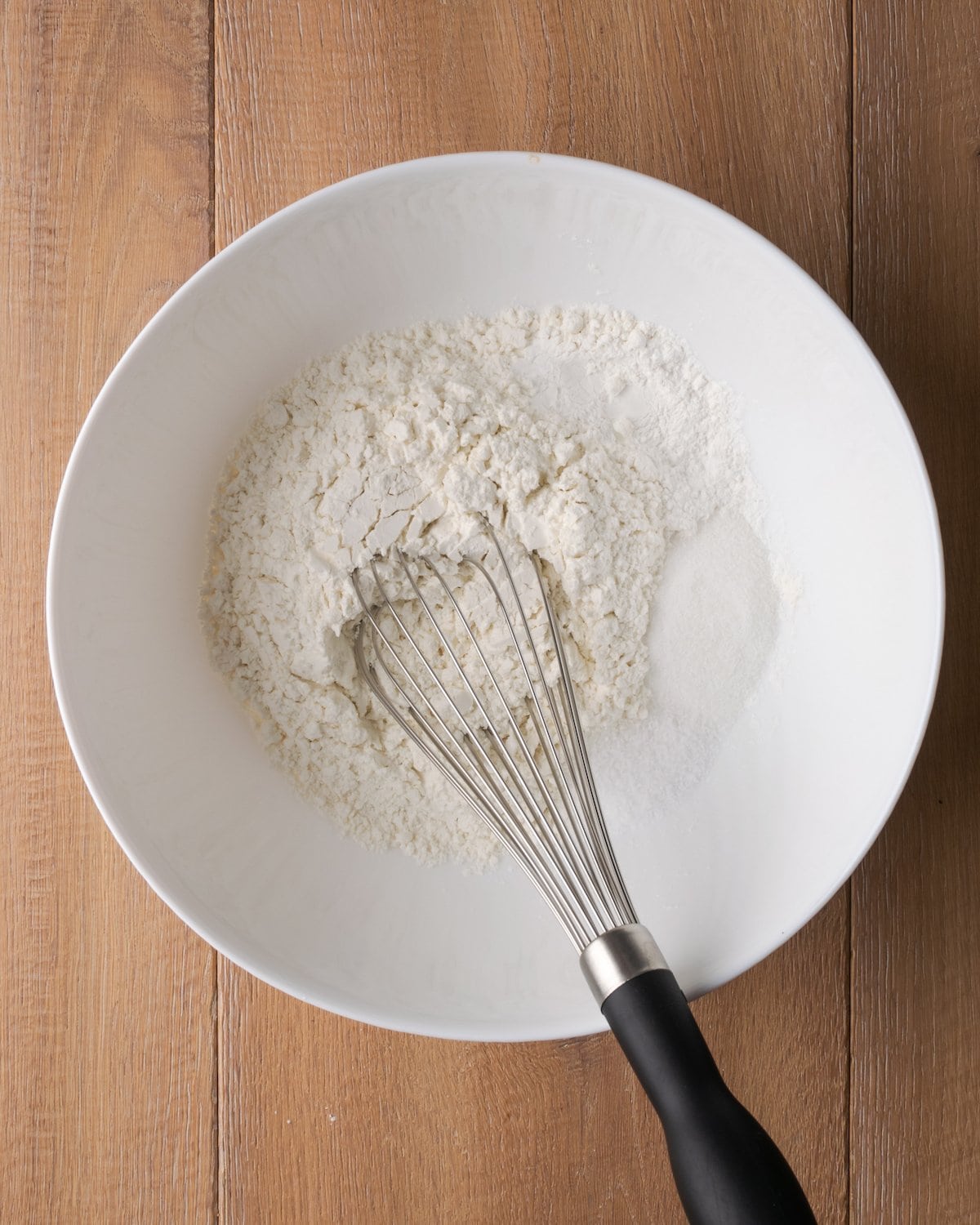 The dry ingredients for butter swim biscuits are whisked together in a white bowl.
