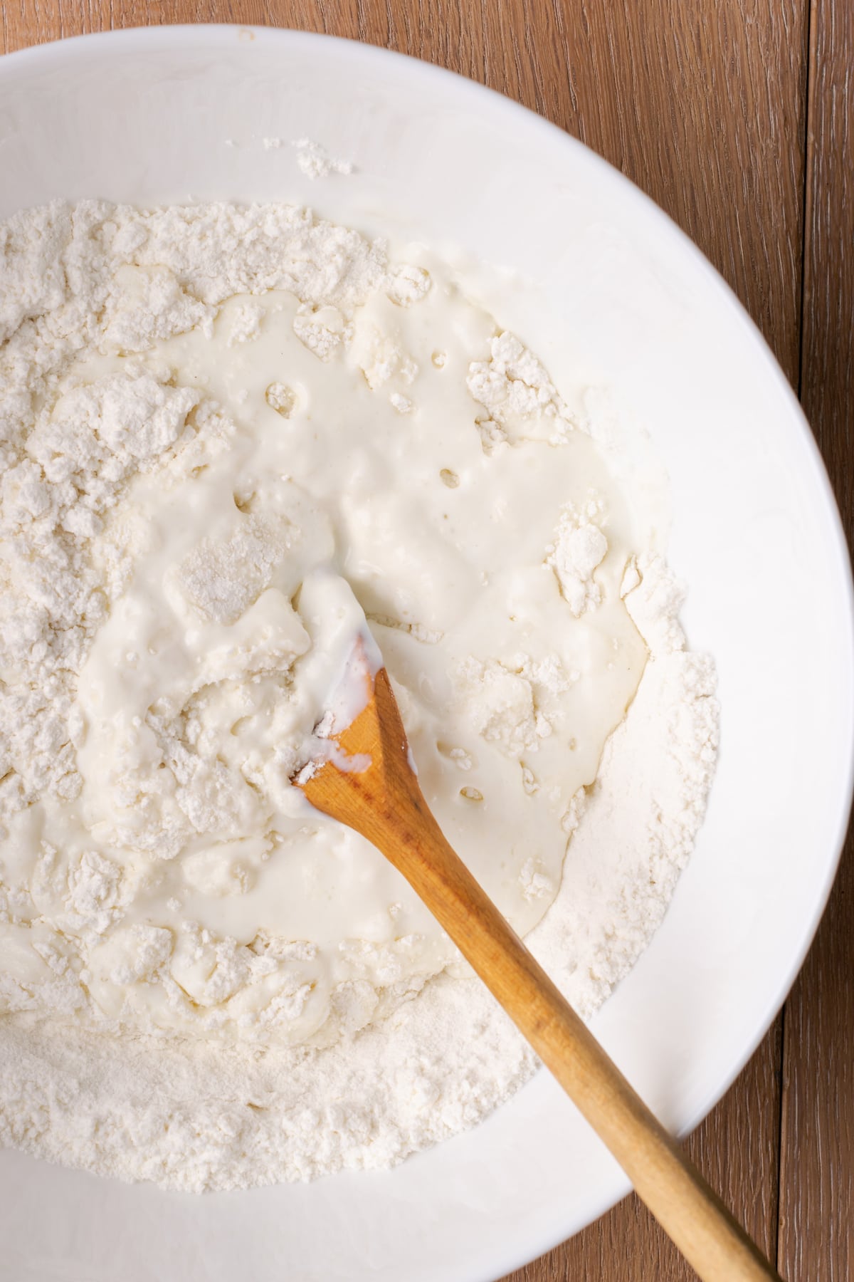 Close up of buttermilk combined with dry ingredients in a bowl with a wooden spoon.