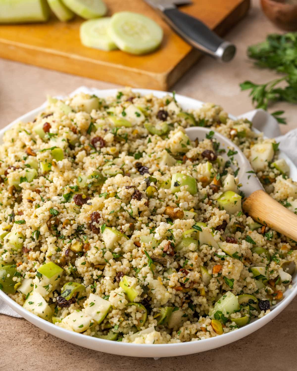 Mediterranean couscous salad in a large white serving dish with a wooden spoon.