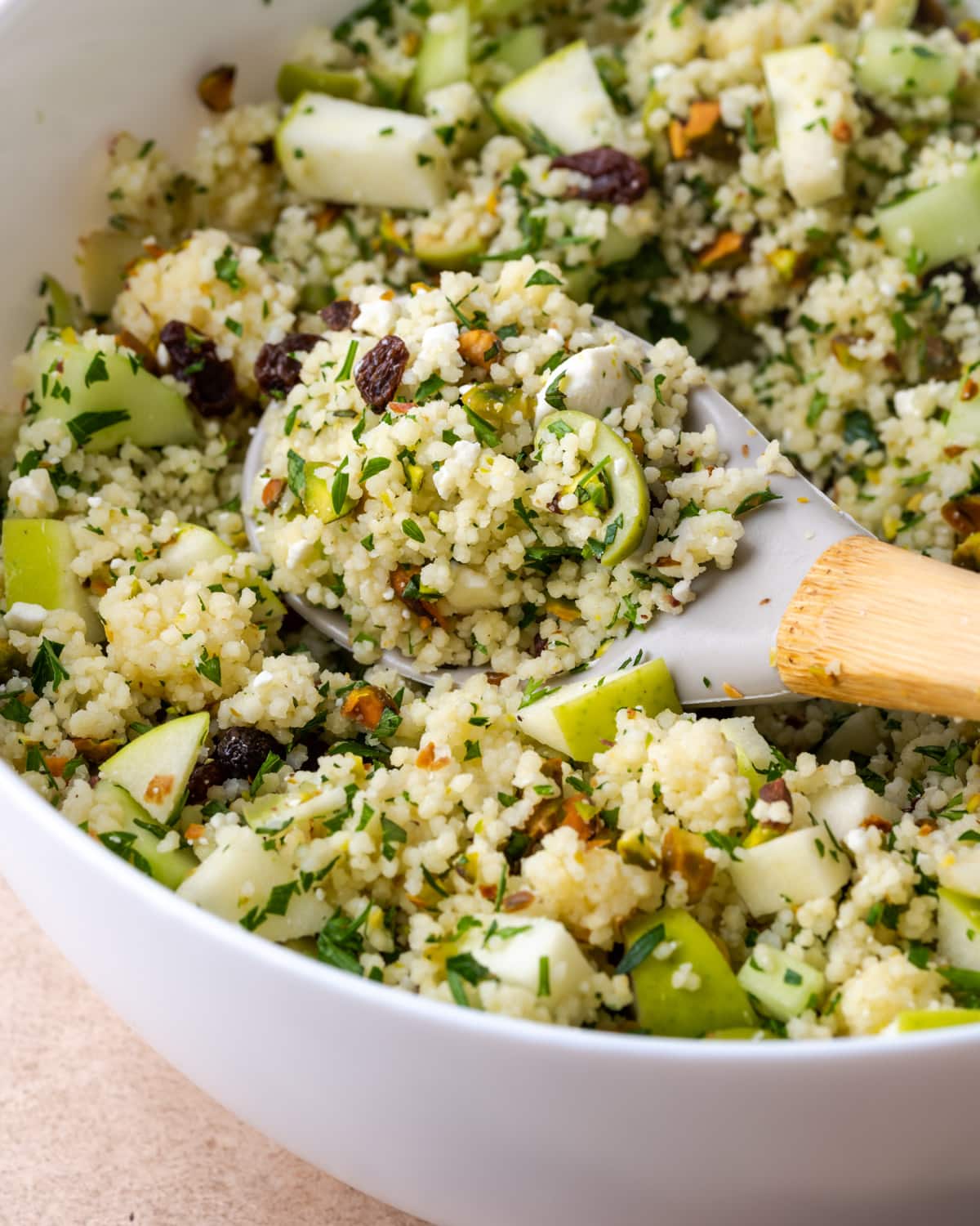 Mediterranean couscous salad in a large white bowl with a wooden spoon.