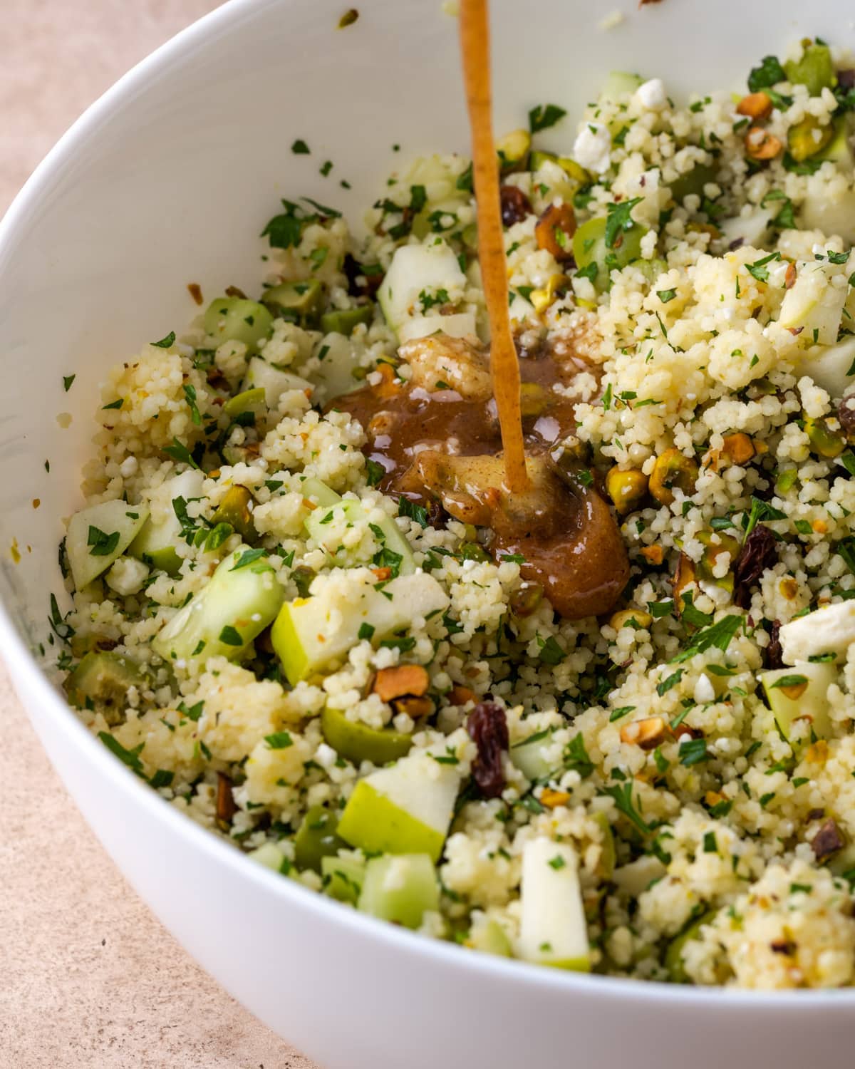 A stream of dressing is drizzled over a bowl of couscous salad.