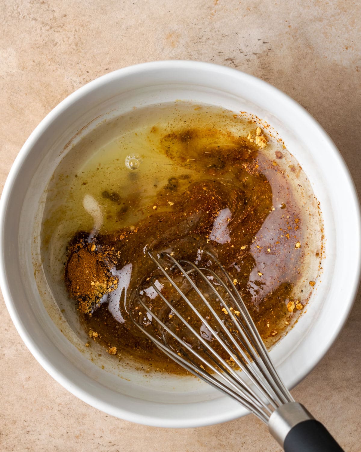 Dressing ingredients are whisked together in a white bowl, with a metal whisk.