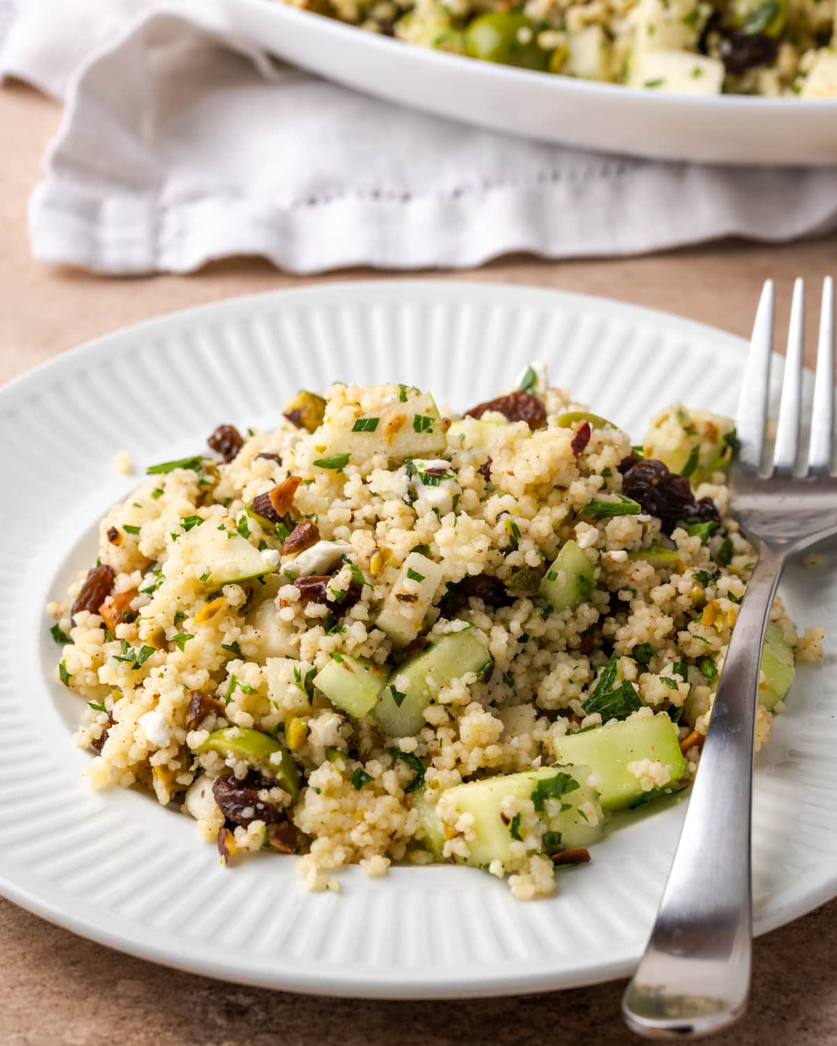 A serving of Mediterranean couscous salad on a white plate with a fork.