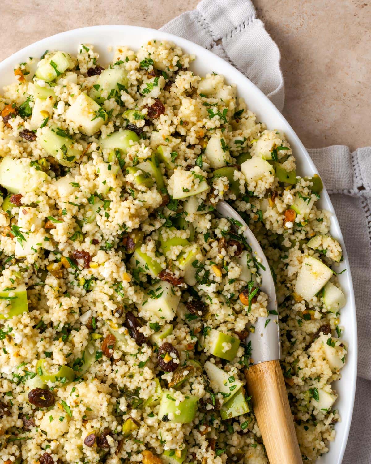Top view of a large platter of Mediterranean couscous salad with a wooden serving spoon.