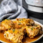 Four instant pot chicken thighs on a plate smothered with gravy.