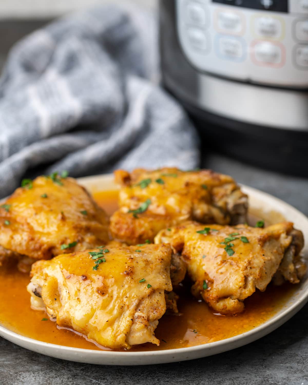 Four instant pot chicken thighs on a plate smothered with gravy.