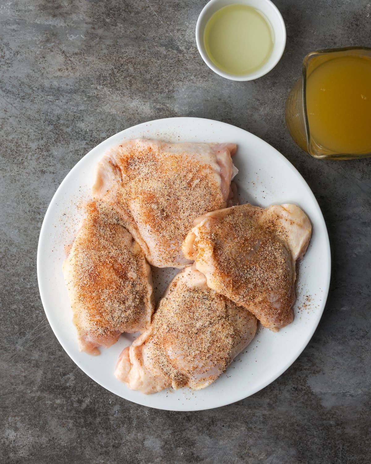 Top view of seasoned uncooked chicken thighs on a white plate.