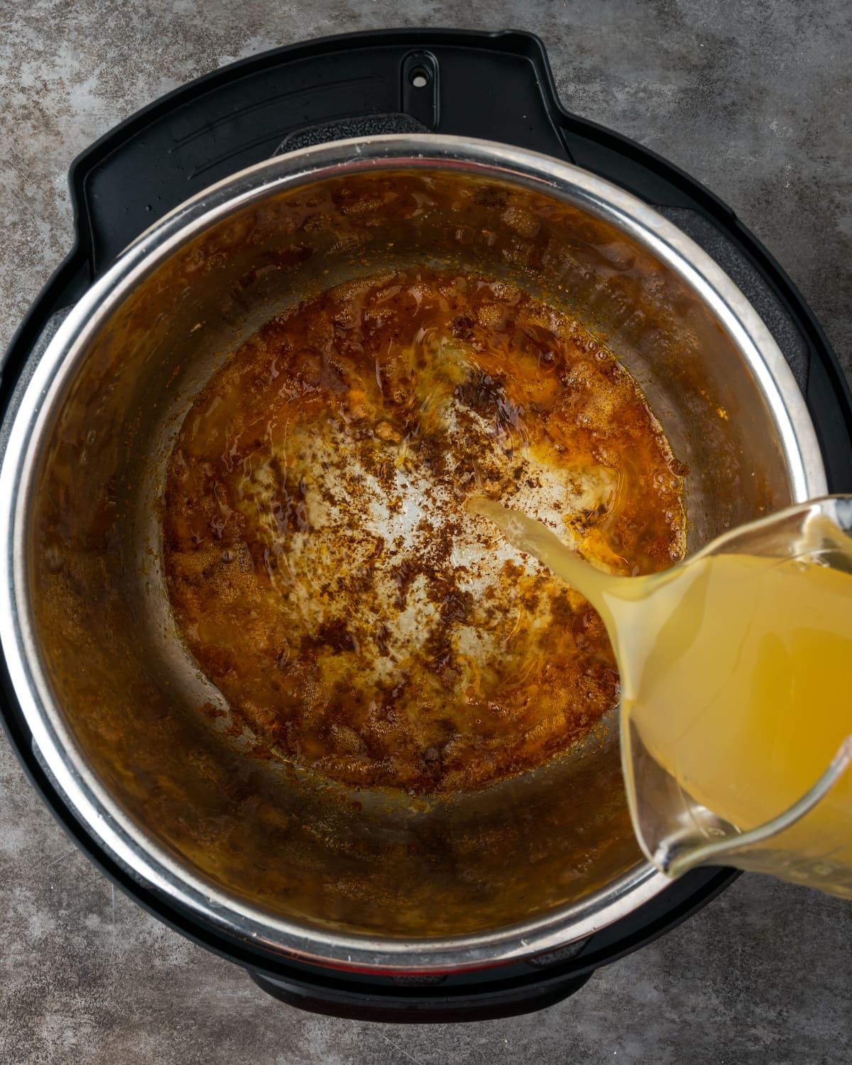 Chicken broth is poured into the instant pot to deglaze.