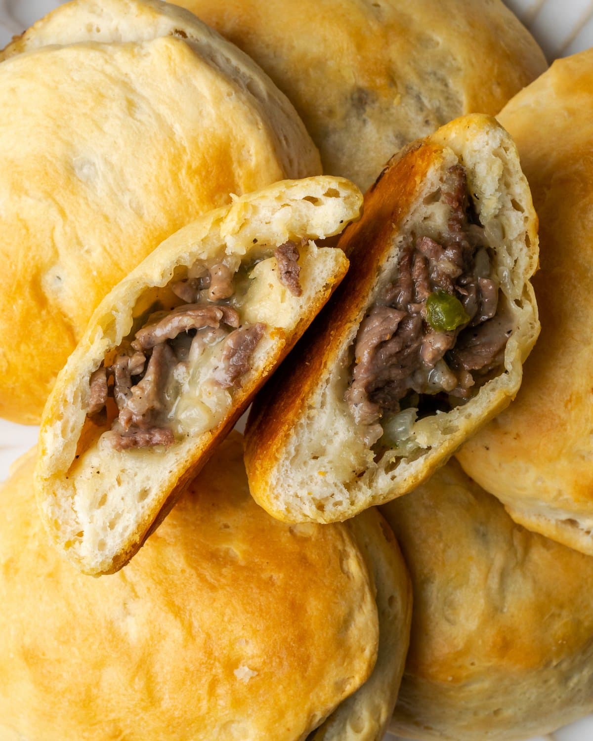 A Philly cheesesteak stuffed biscuit cut in half, surrounded by more stuffed biscuits.