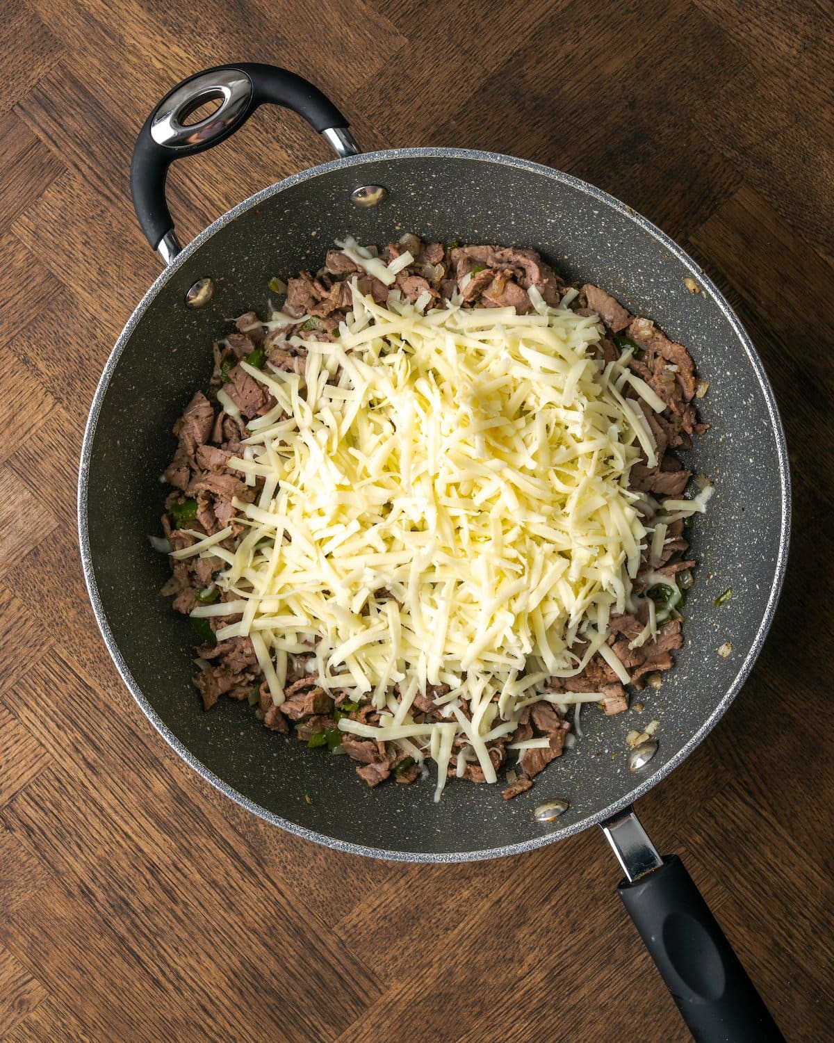 Shredded cheese added to a skillet with Philly cheesesteak mixture.