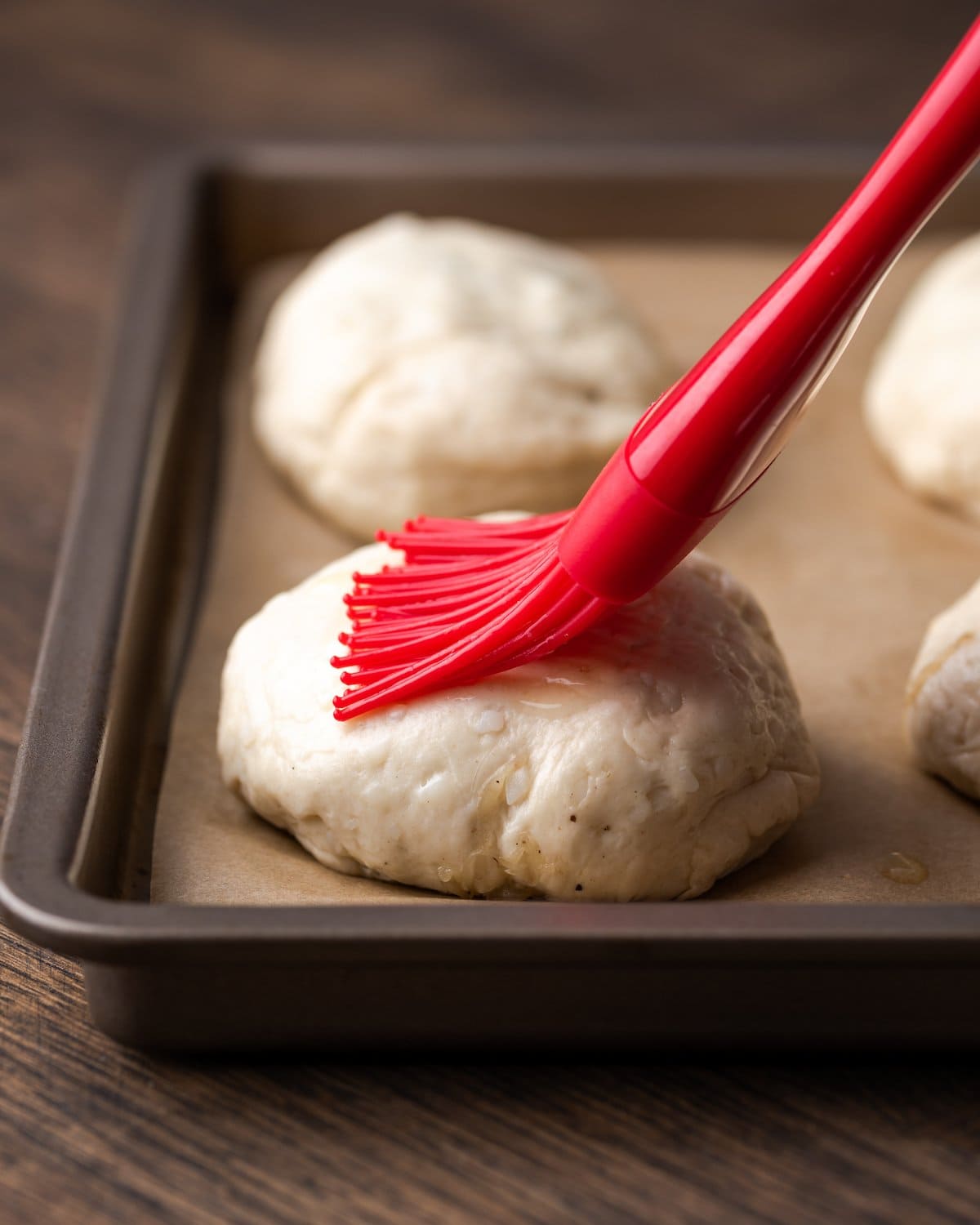 A silicone brush brushes melted butter over top a Philly cheesesteak stuffed biscuit.