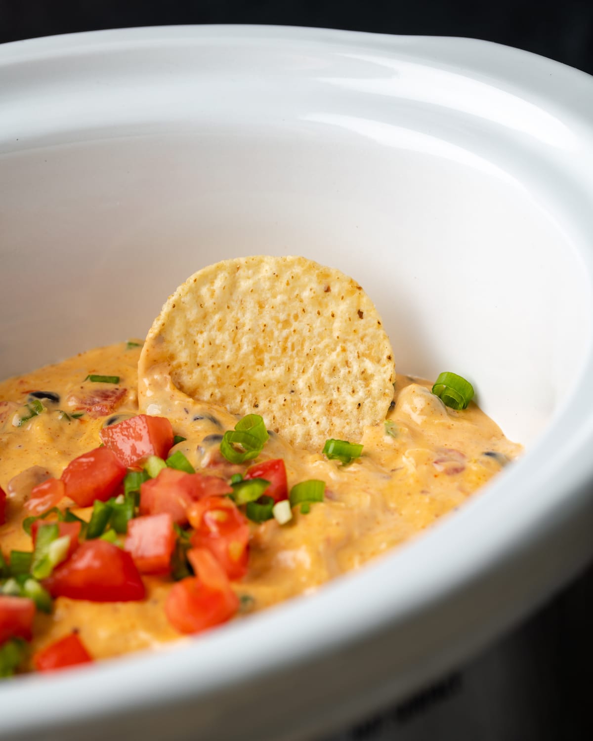 Close-up of a nacho chip dipped in cheesy chicken nacho dip in a crock pot.