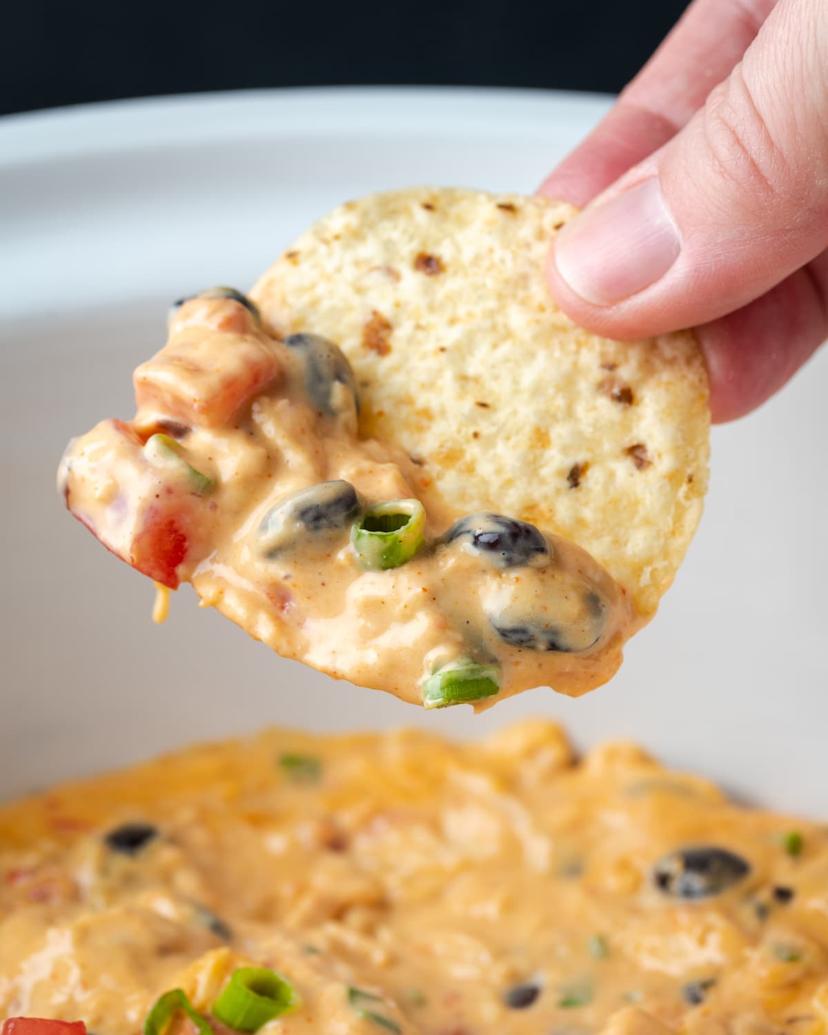 A hand holding a chip dipped in Crock Pot chicken nacho dip.