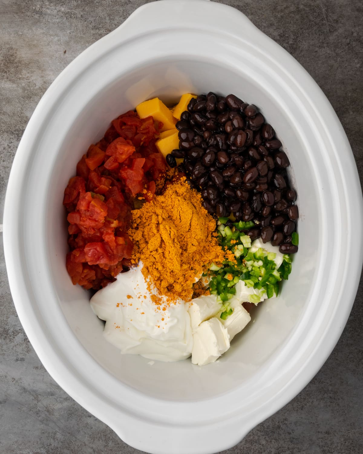 Overhead view of chicken nacho dip ingredients assembled in a crock pot bowl.